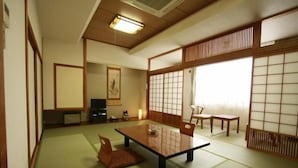 A traditional Japanese room with tatami flooring, a low table with cushions, sliding doors, and a television. - Hiraizumi Hotel Musashibou (Hiraizumi)