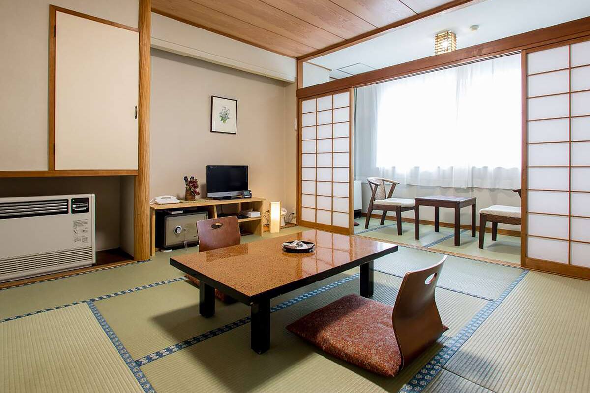 A traditional Japanese room with tatami flooring, a low table, chairs, a TV, and sliding doors.
