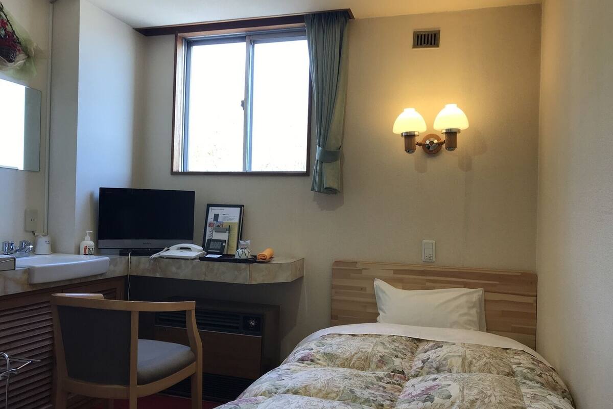 A hotel room with a bed, desk, chair, and a window with curtains.