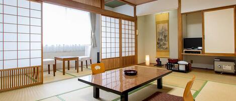 A traditional Japanese room with tatami flooring, a low table, chairs, a television, and a cabinet.