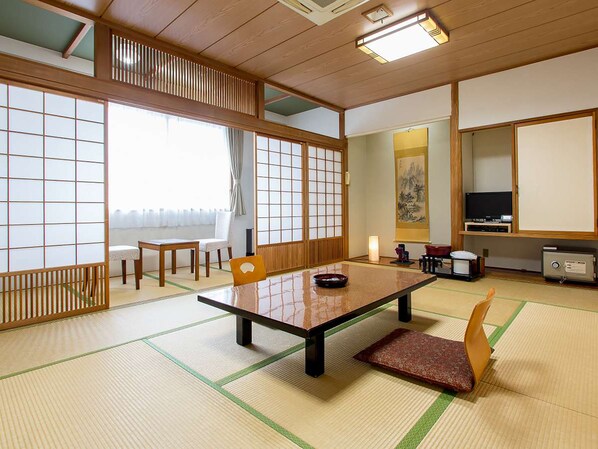 Una habitación japonesa tradicional con suelo de tatami, una mesa baja, sillas, un televisor y un armario.