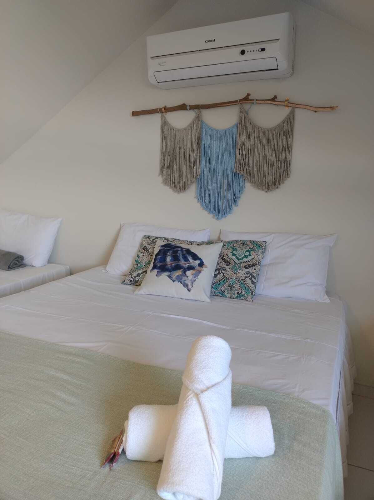 Quarto com cama, almofadas, toalha, ar condicionado e decoração nas paredes.