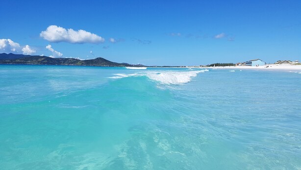 A beach with clear turquoise water, a sandy shore, and distant hills. - Terra Nova Cabo Frio Front Beach (Cabo Frio)