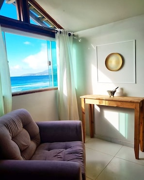 A room with a view of the ocean, a cushioned chair, a wooden table, and a decorative plate on the wall. - Terra Nova Cabo Frio Front Beach (Cabo Frio)