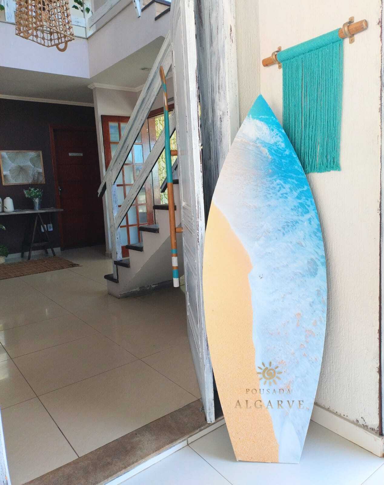 A surfboard leaning against a wall in a room with a staircase and a hanging hammock.