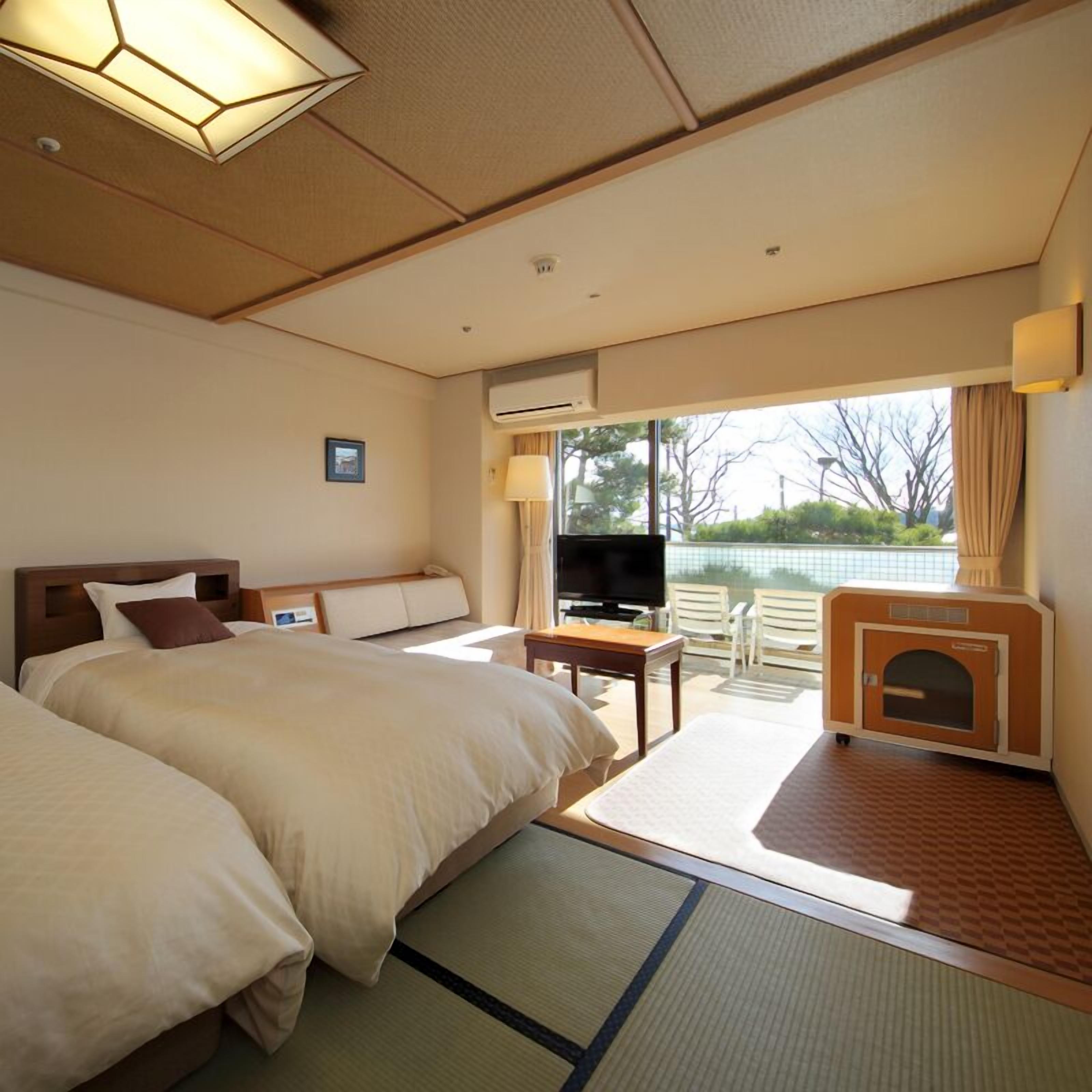 A hotel room with two beds, a television, a small table, and a view of the outdoors.