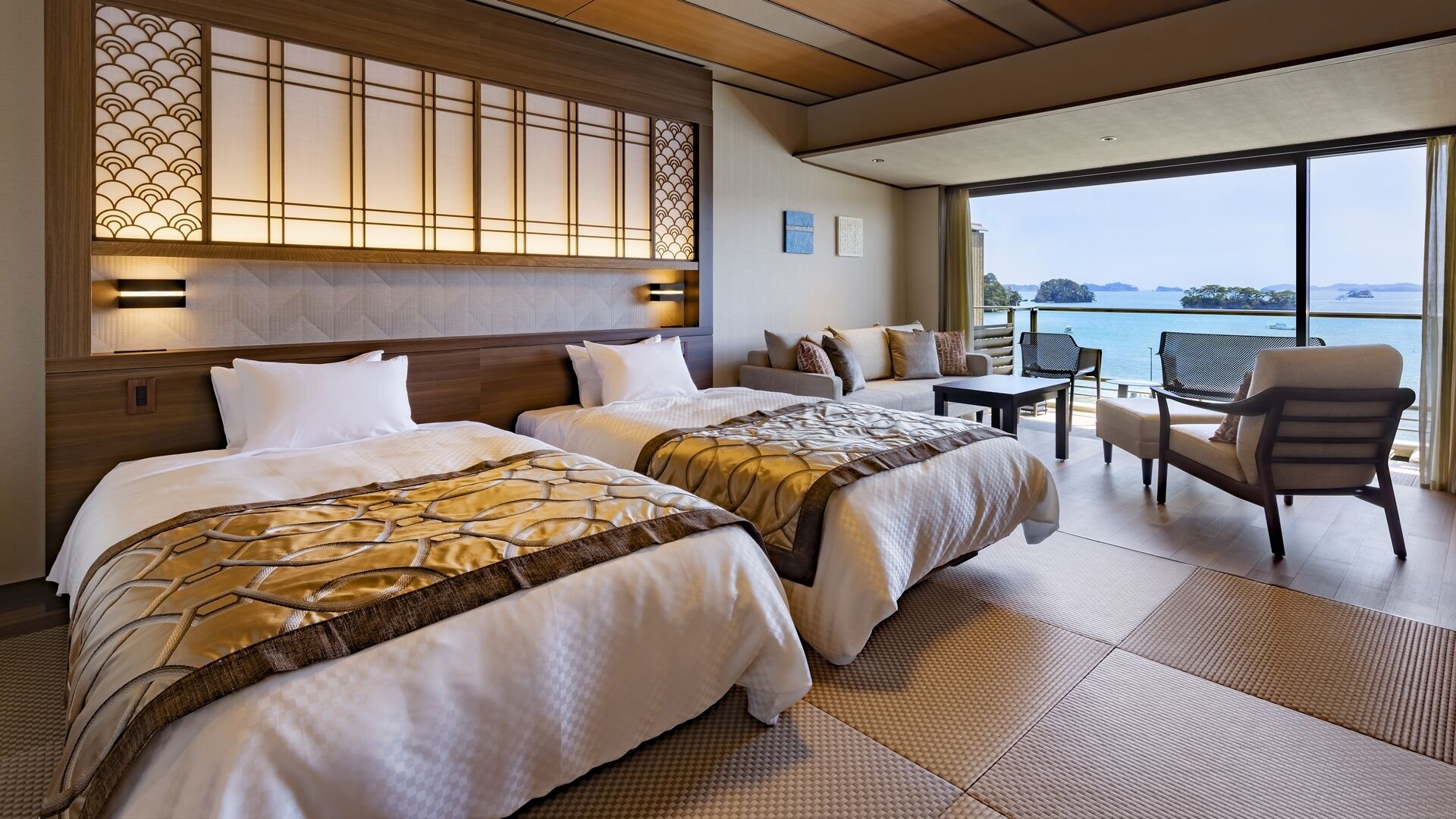 A hotel room with two beds, a sofa, a table, and a view of the sea.