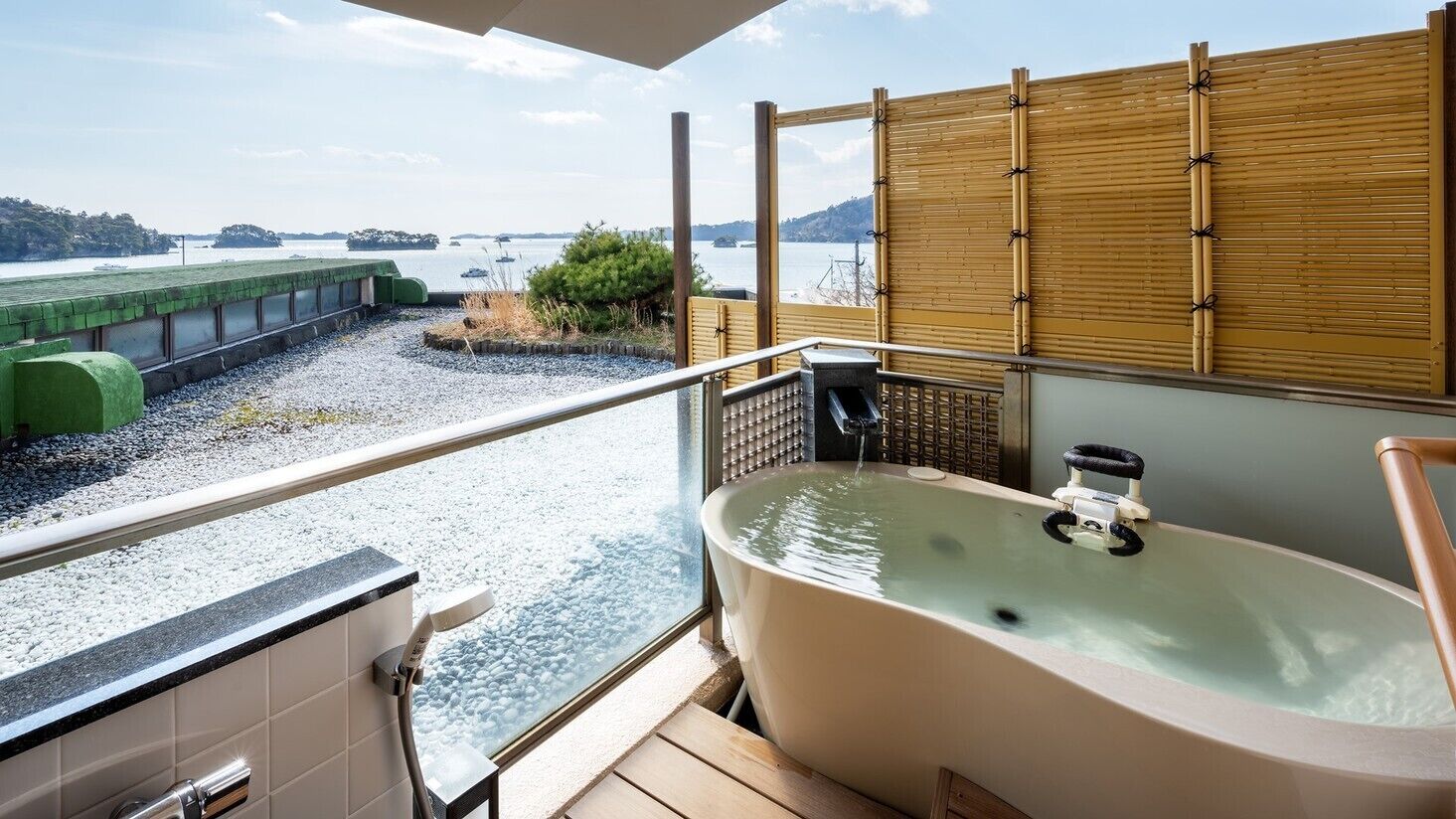 A balcony with a view of a body of water, a hot tub, and a bamboo screen.