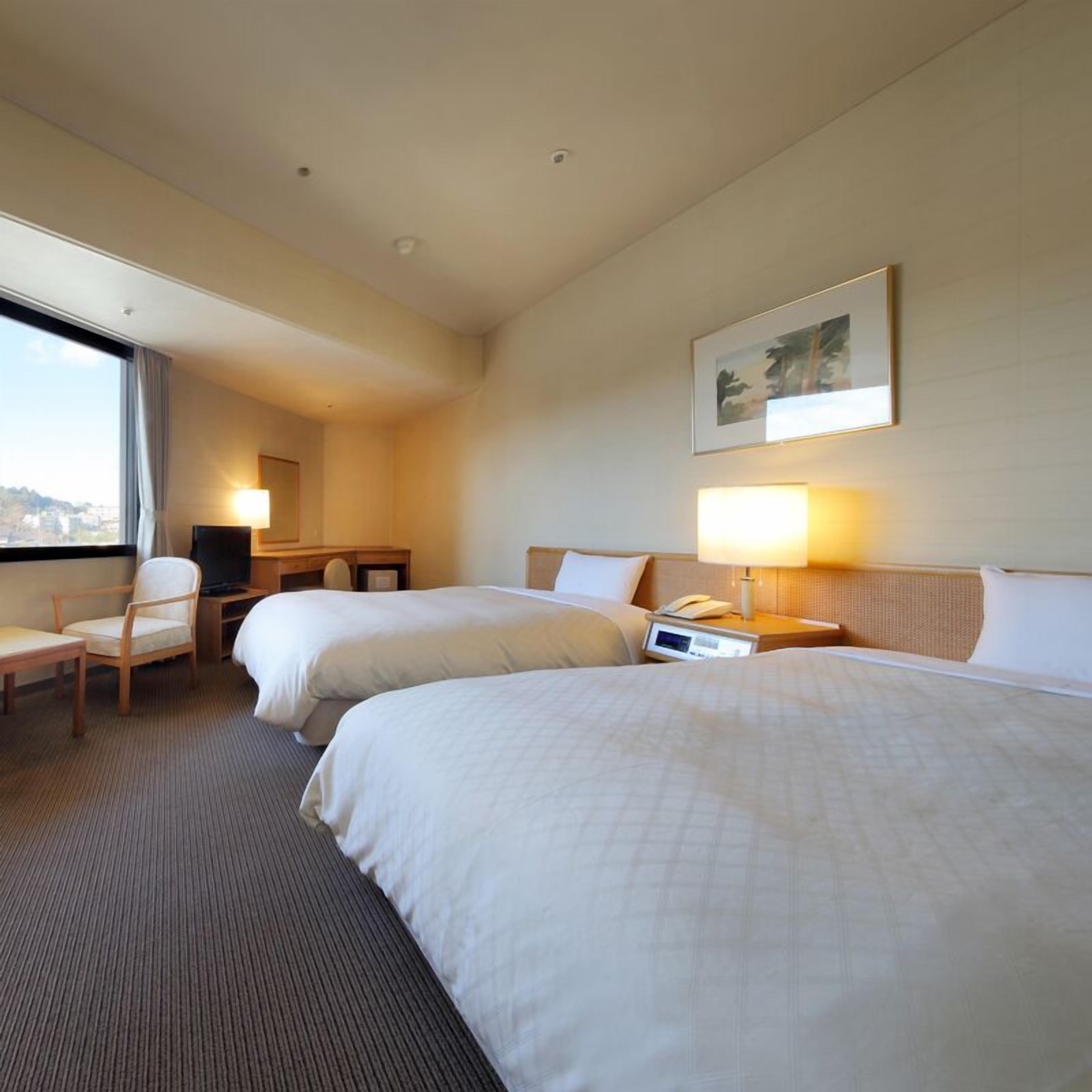 A hotel room with two beds, a desk, a chair, a TV, and a window with a view.