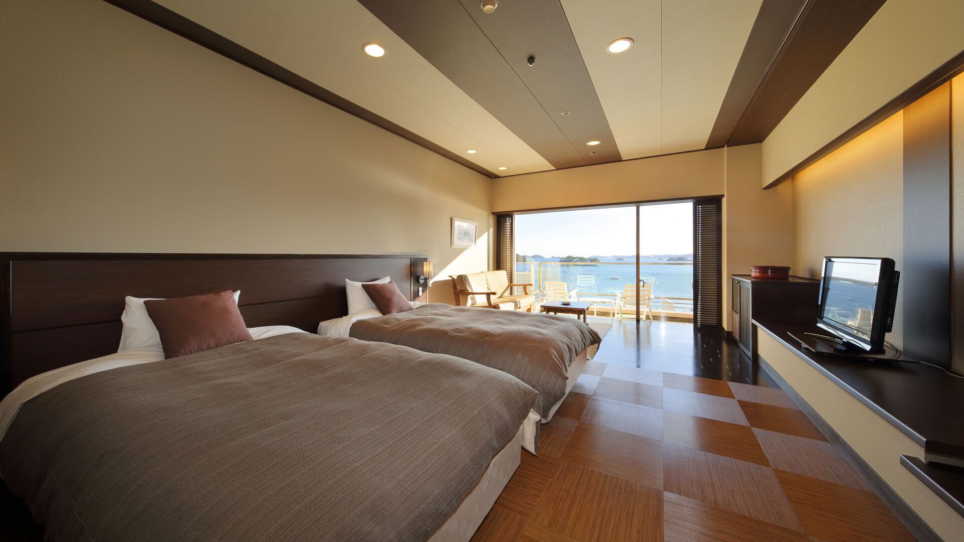 A hotel room with two beds, a TV, and a view of the sea.