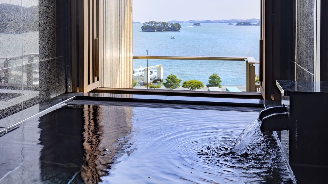 A modern bathroom with a large bathtub, a view of the sea, and a wooden panel wall.