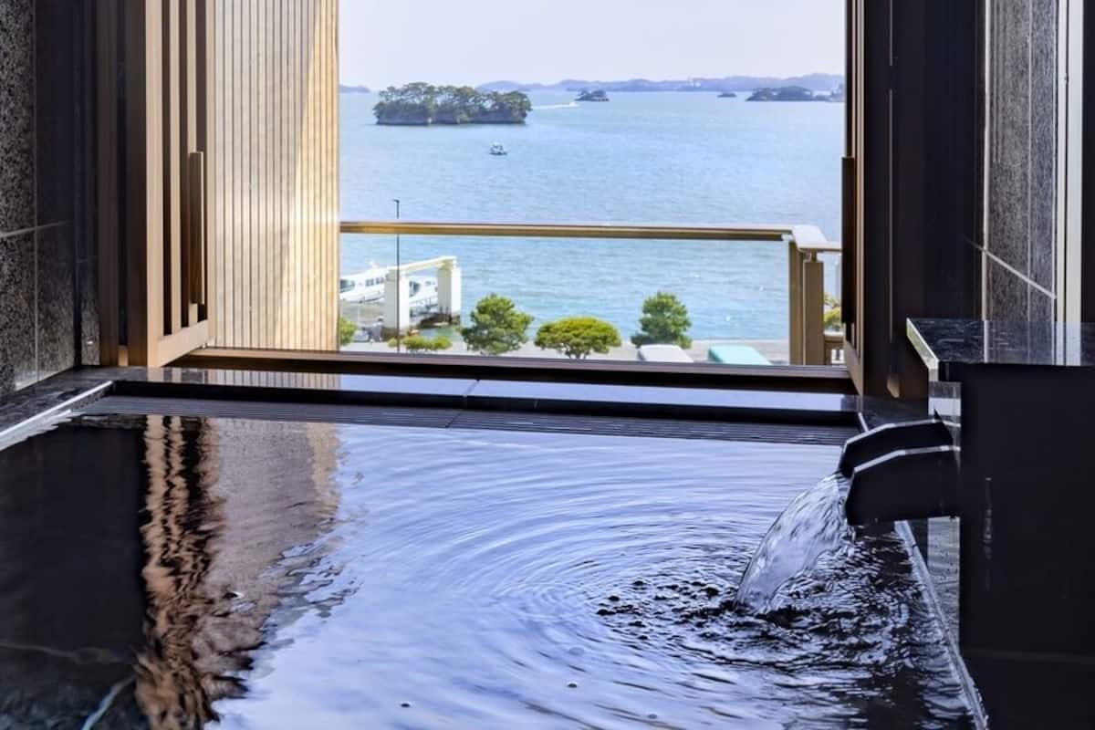 Un baño moderno con una bañera grande, vistas al mar y un revestimiento de pared de madera.