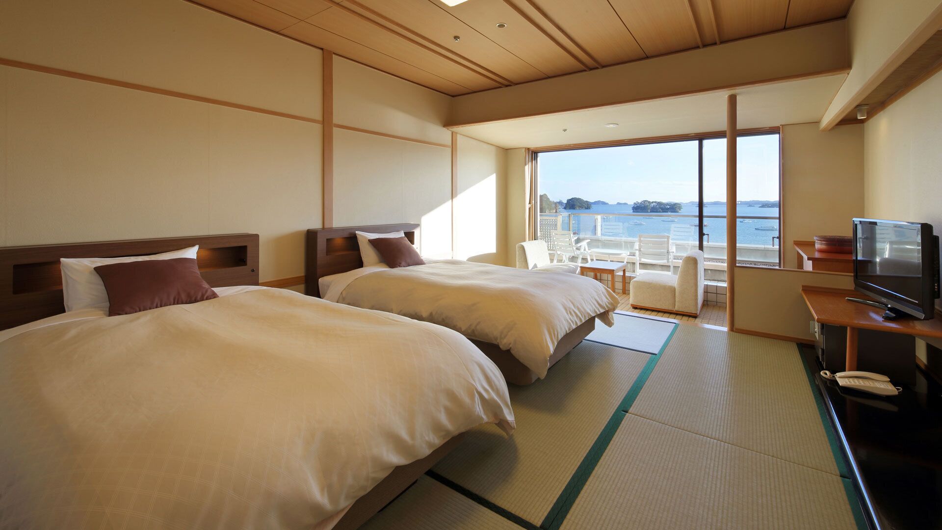 A hotel room with two beds, a TV, and a view of the sea.
