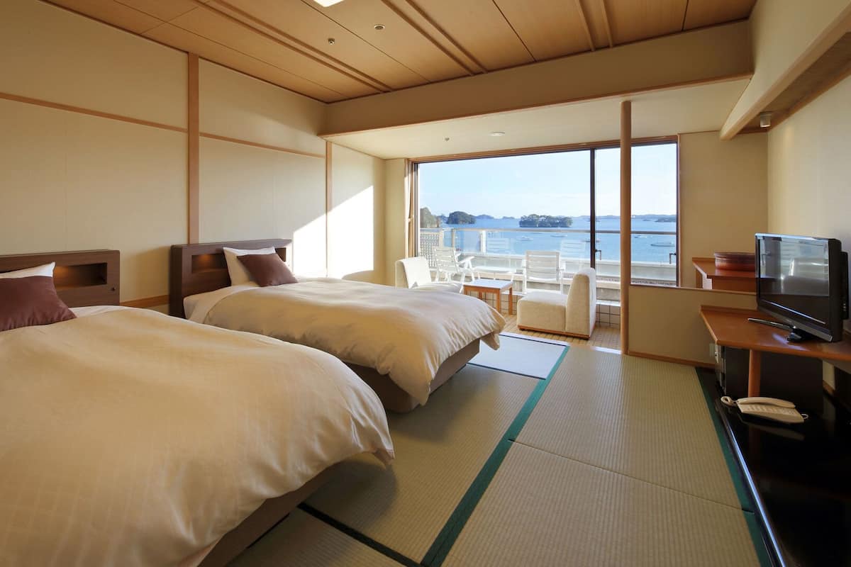 Habitación de hotel con dos camas, televisión y vista al mar.