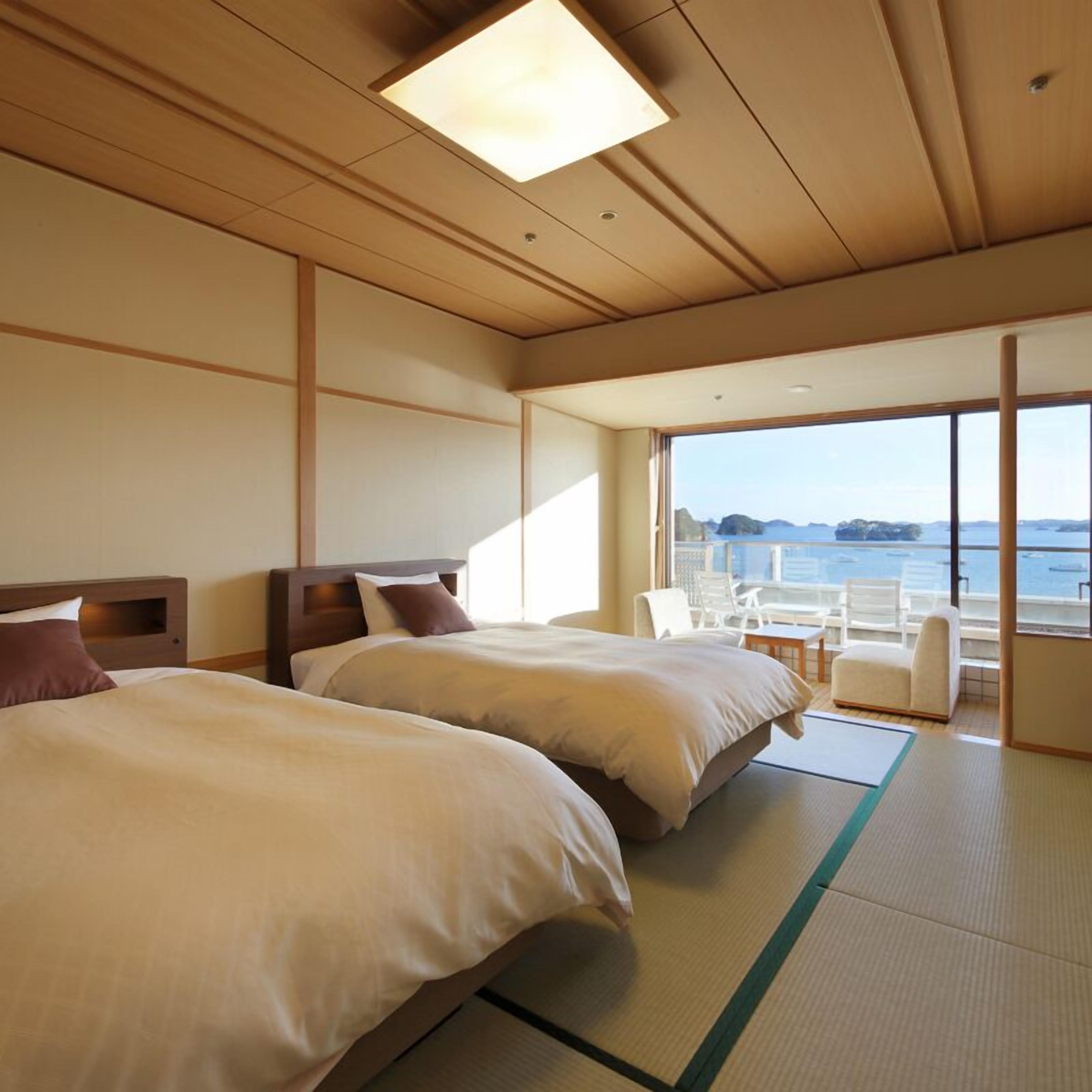 A hotel room with two beds, a large window with a view of the sea, and a small seating area.