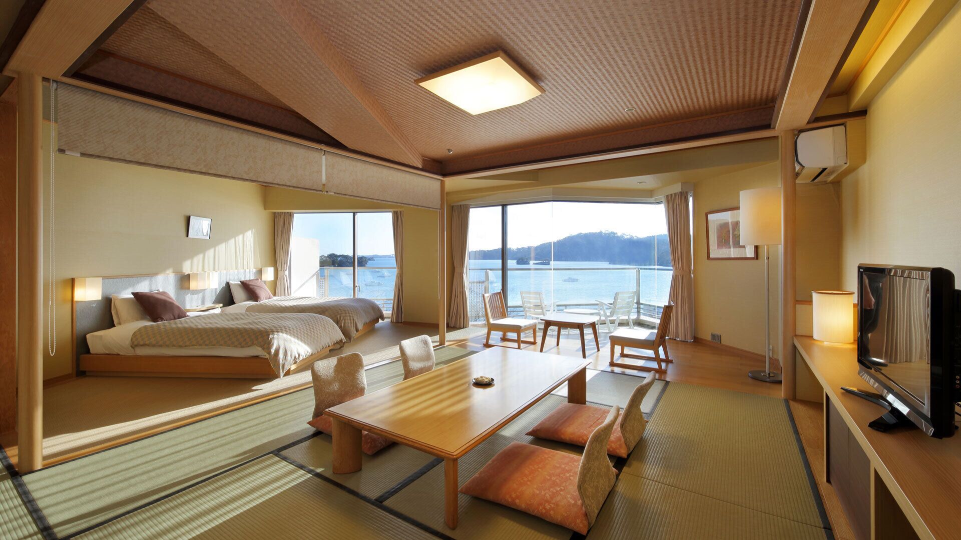 A hotel room with a bed, a dining table, chairs, a TV, and a view of the sea.