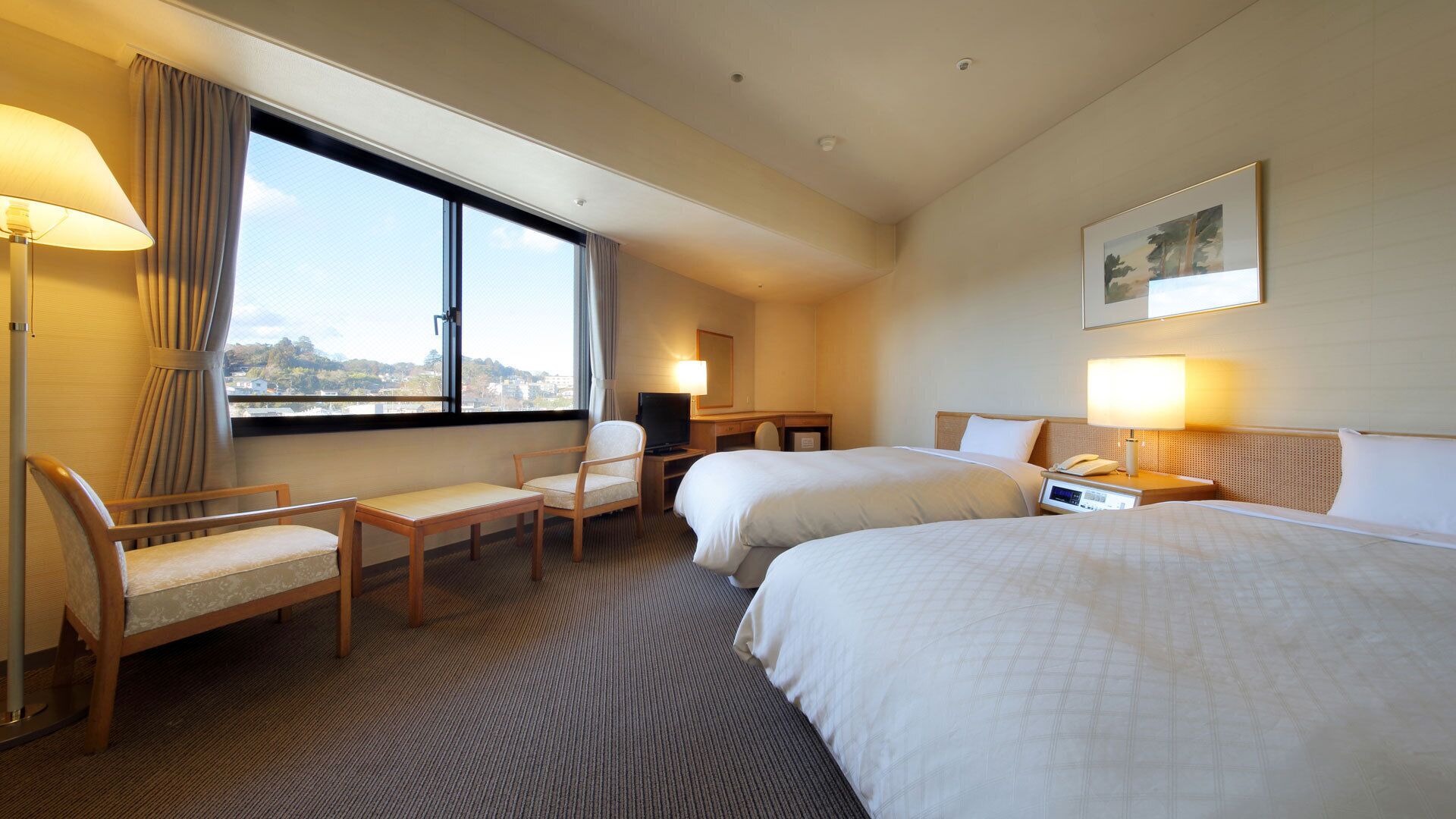 A hotel room with two beds, a desk, a chair, a TV, and a window with a view.