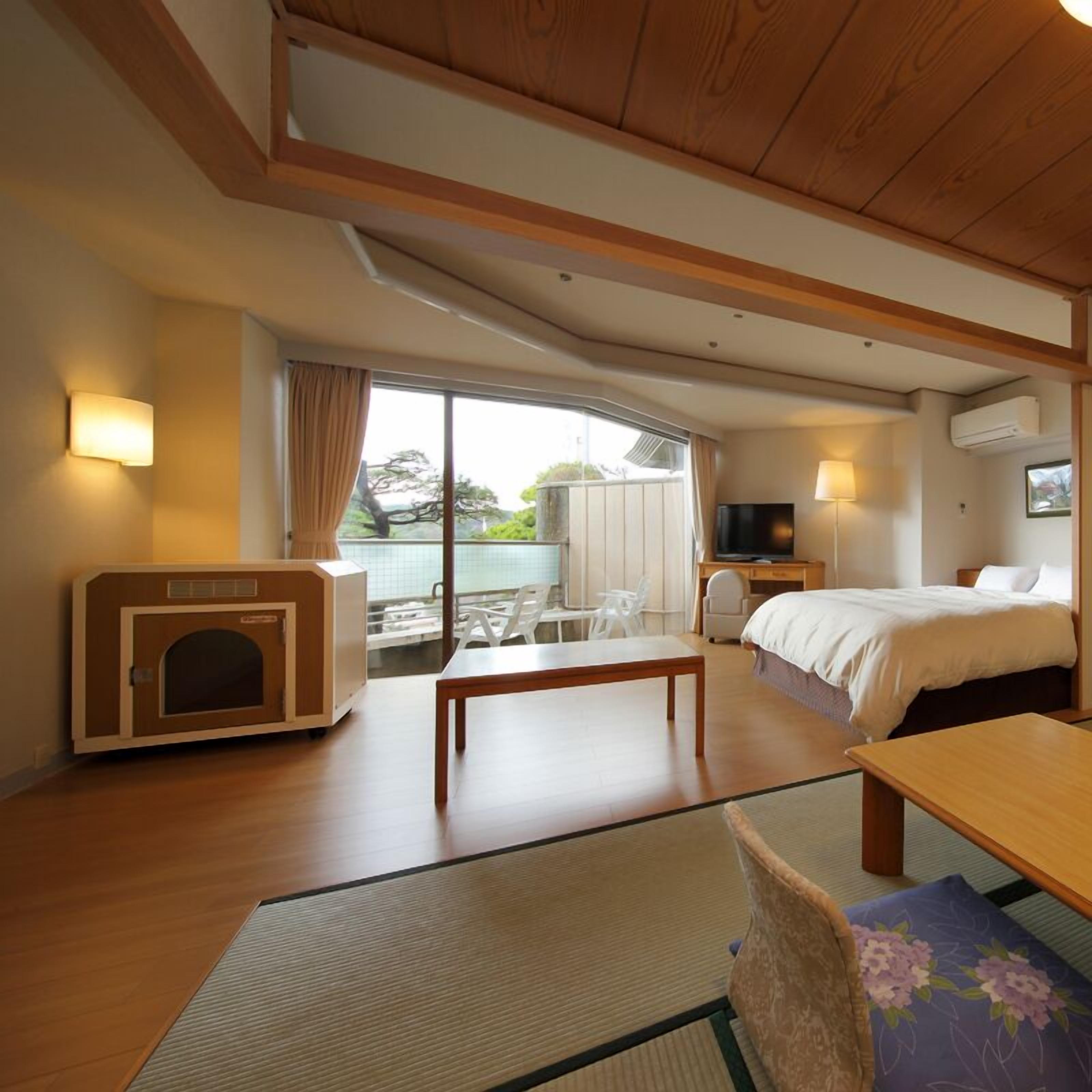 A hotel room with a bed, a TV, a fireplace, a dining table, and a view of the outdoors.