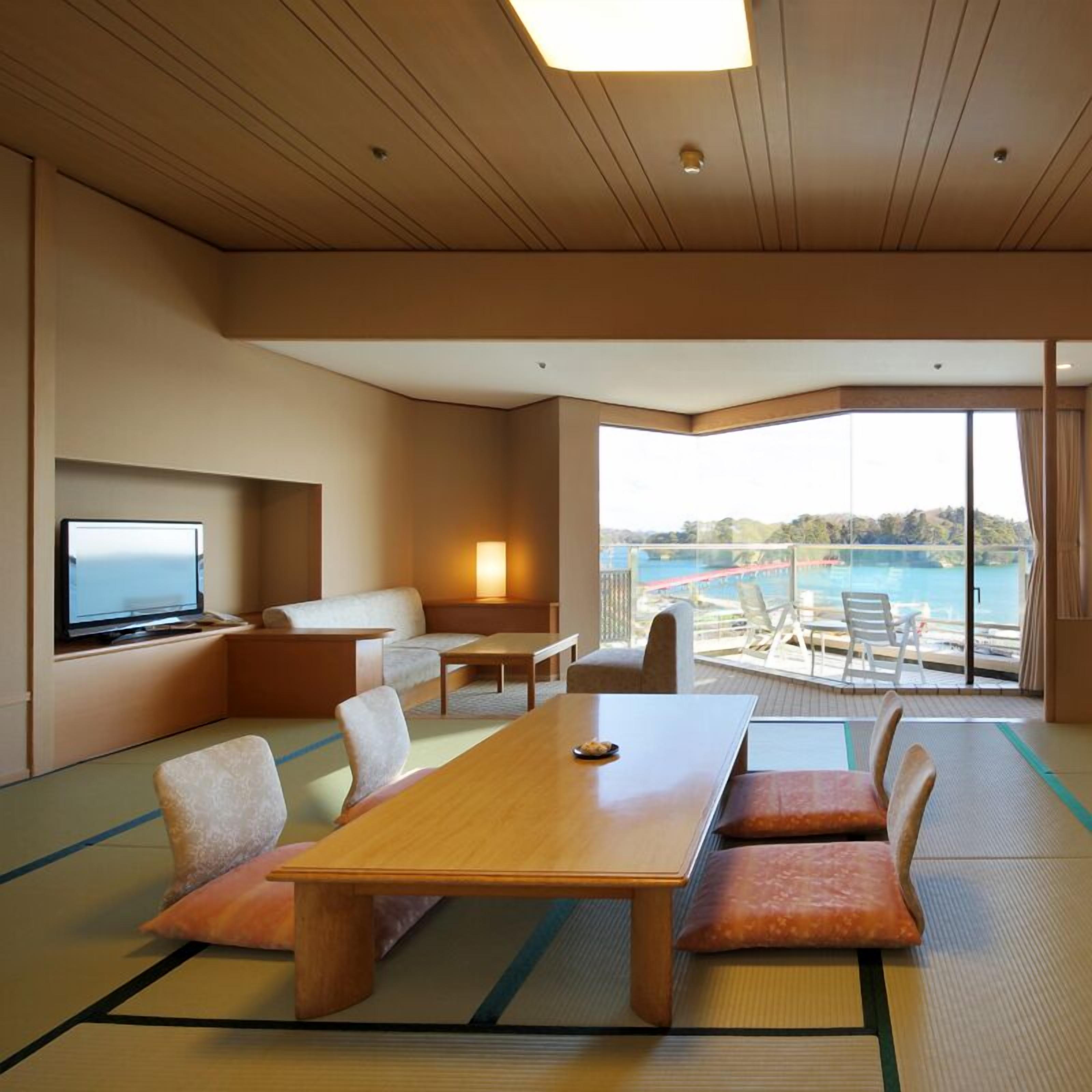 A modern hotel room with a large window, a flat-screen TV, a sofa, a dining table, and tatami mats.