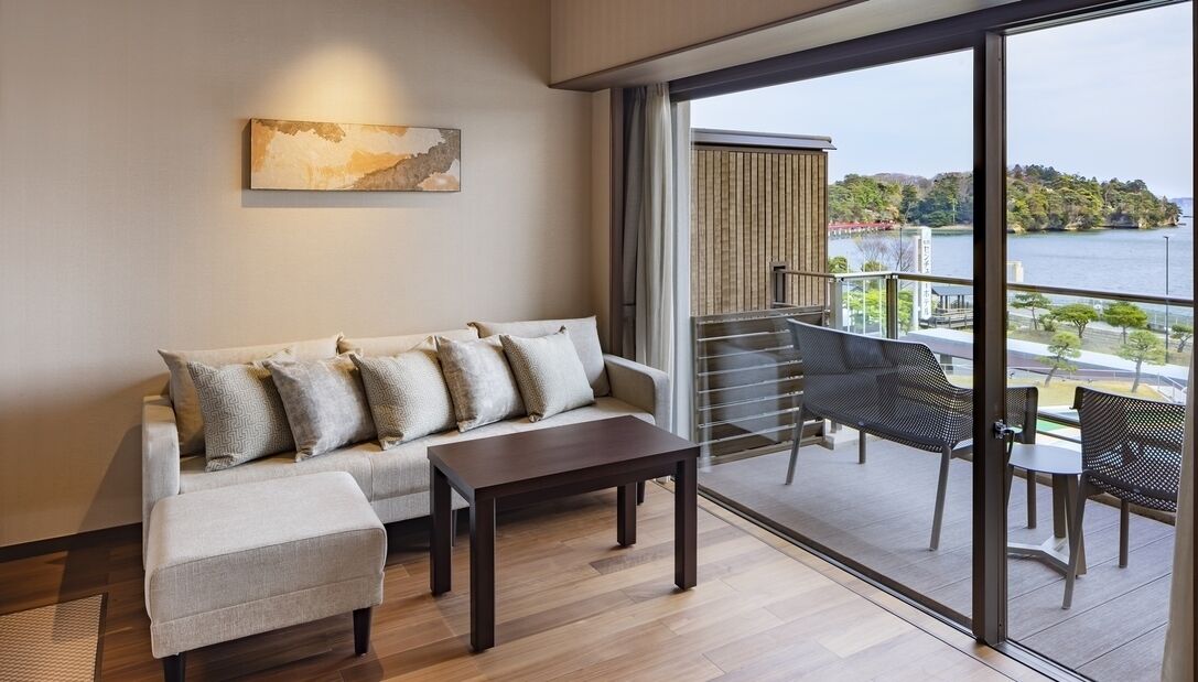 A modern living room with a sofa, a table, and a balcony with outdoor furniture.
