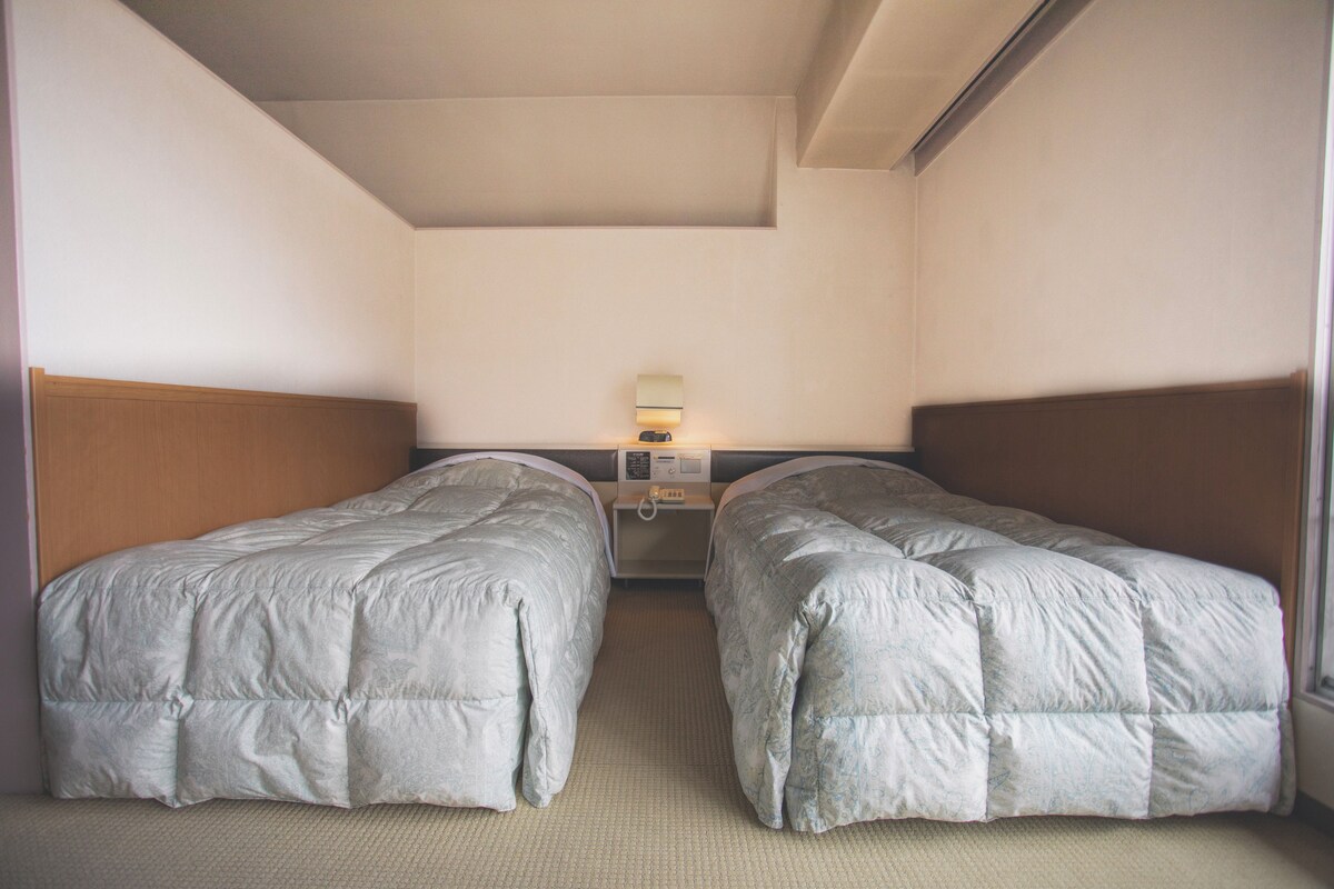 A room with two single beds, a bedside table with a lamp, and a window.