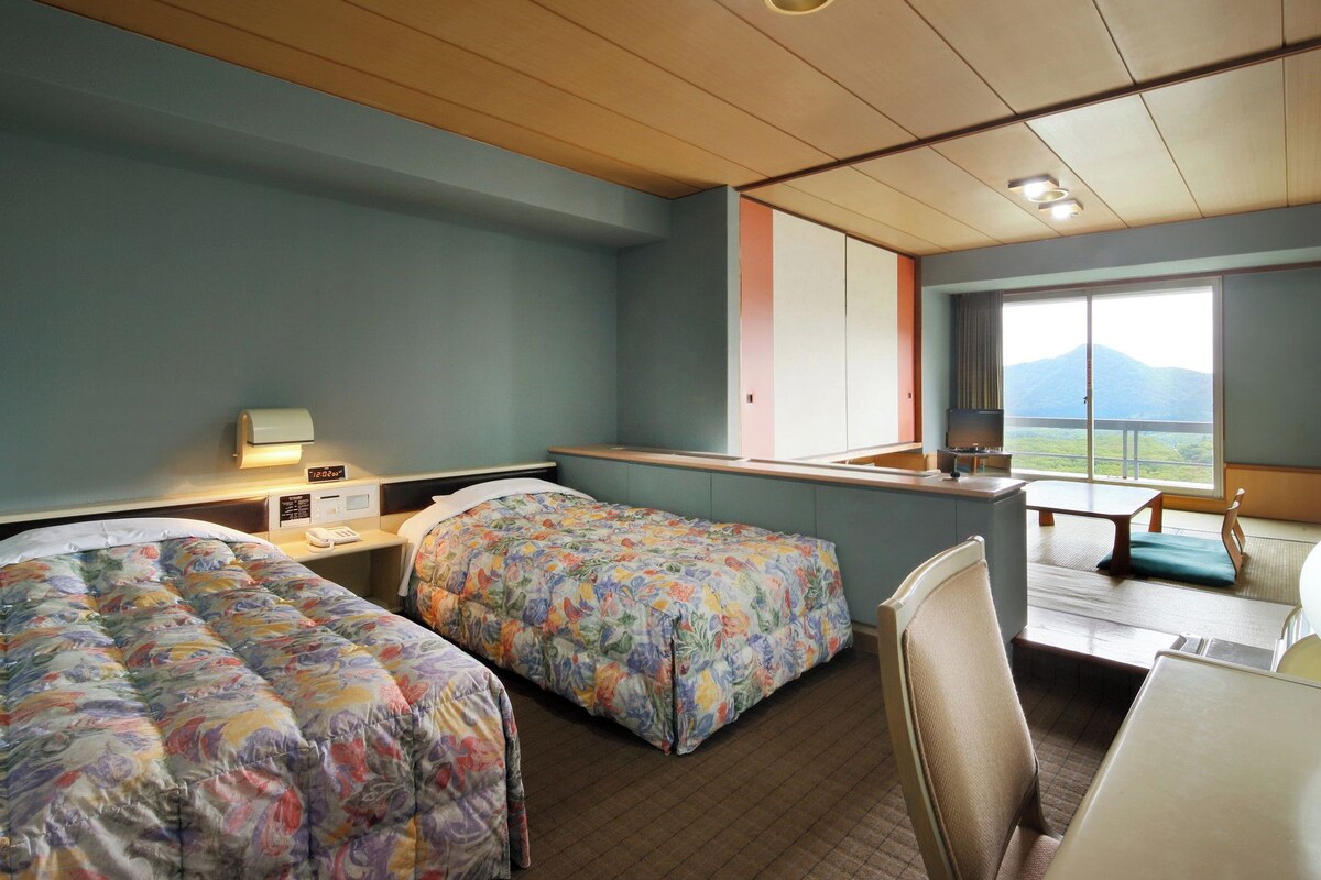 A hotel room with two beds, a desk, a chair, a television, and a window with a view of mountains.