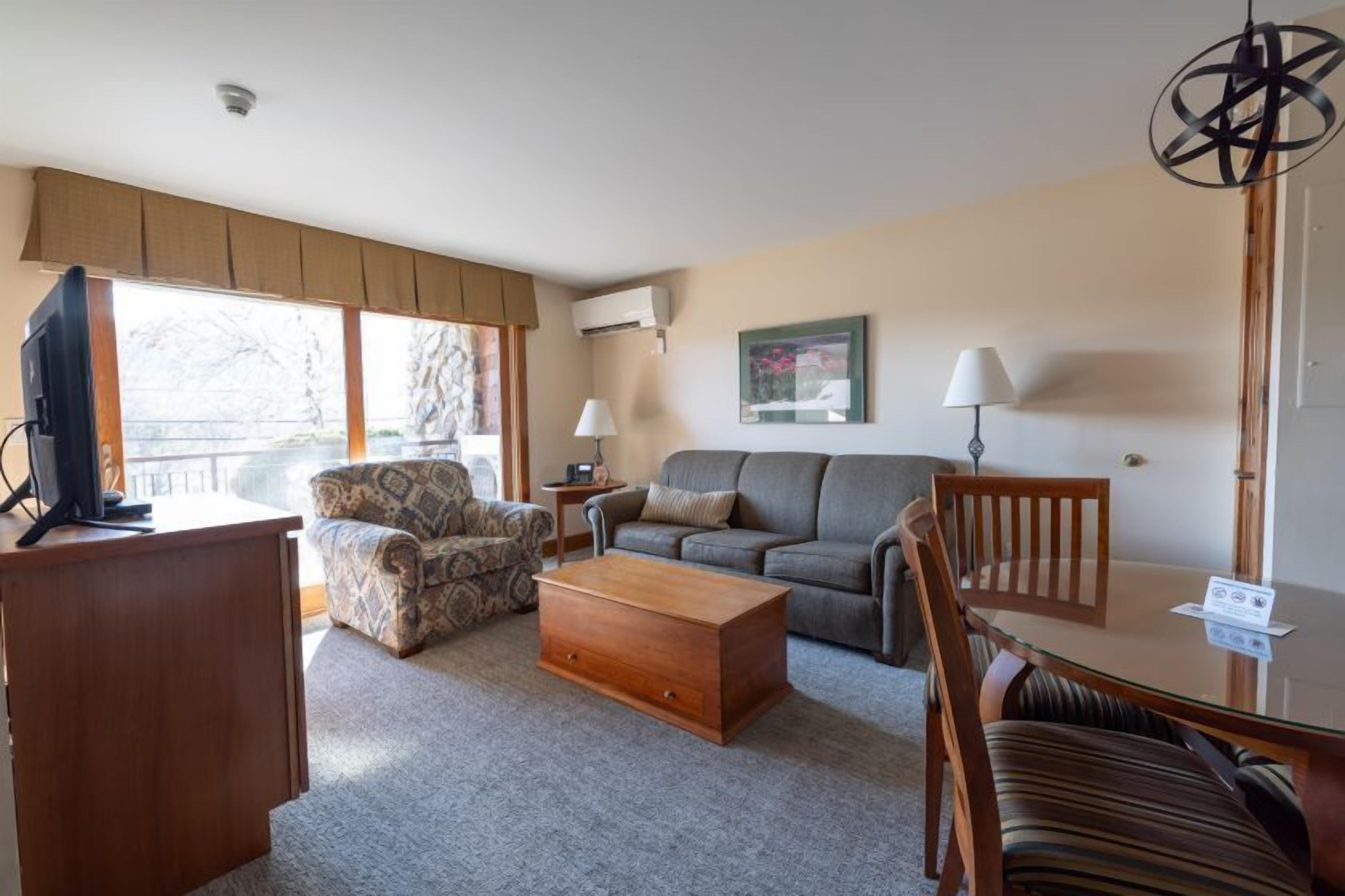 Un salon comprenant un canapé, un fauteuil, une table basse, un téléviseur et une table à manger avec des chaises.