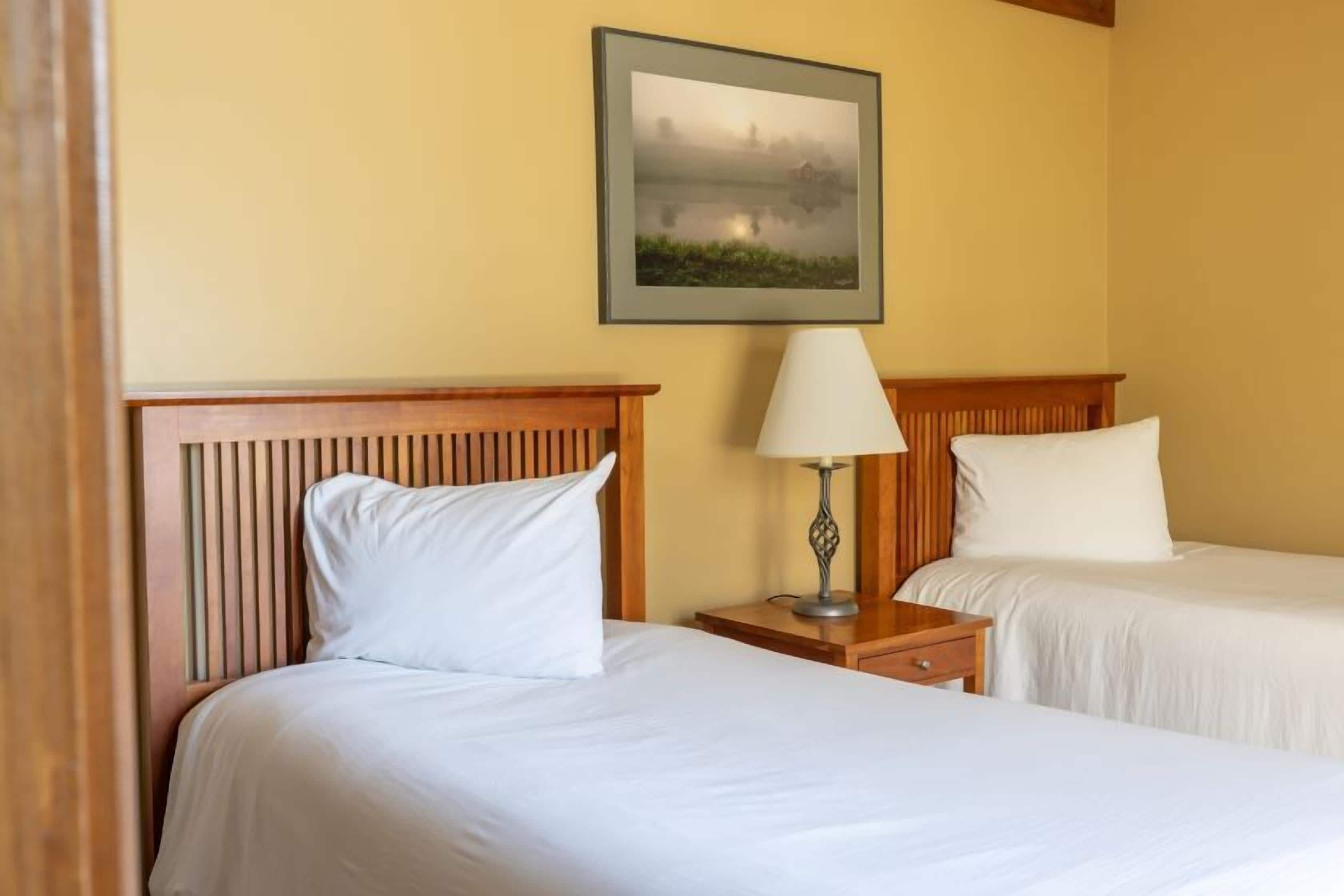 Een hotelkamer met twee bedden, een nachtkastje met een lamp en een lijst aan de muur.