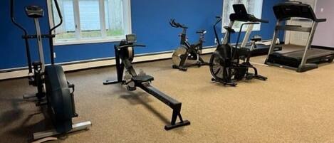 A gym with various exercise equipment including a treadmill, stationary bikes, and a rowing machine.