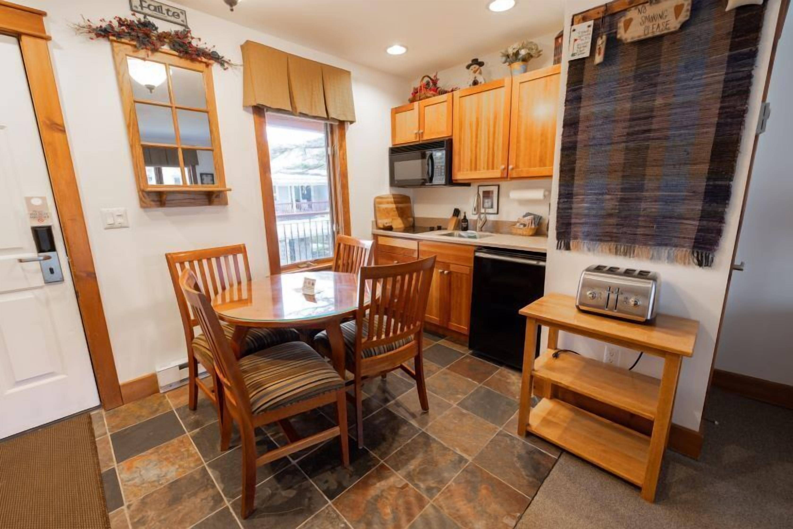 A compact kitchen with wooden cabinets, a microwave, a toaster, and a dining table with chairs.