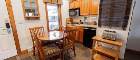 A compact kitchen with wooden cabinets, a microwave, a toaster, and a dining table with chairs.