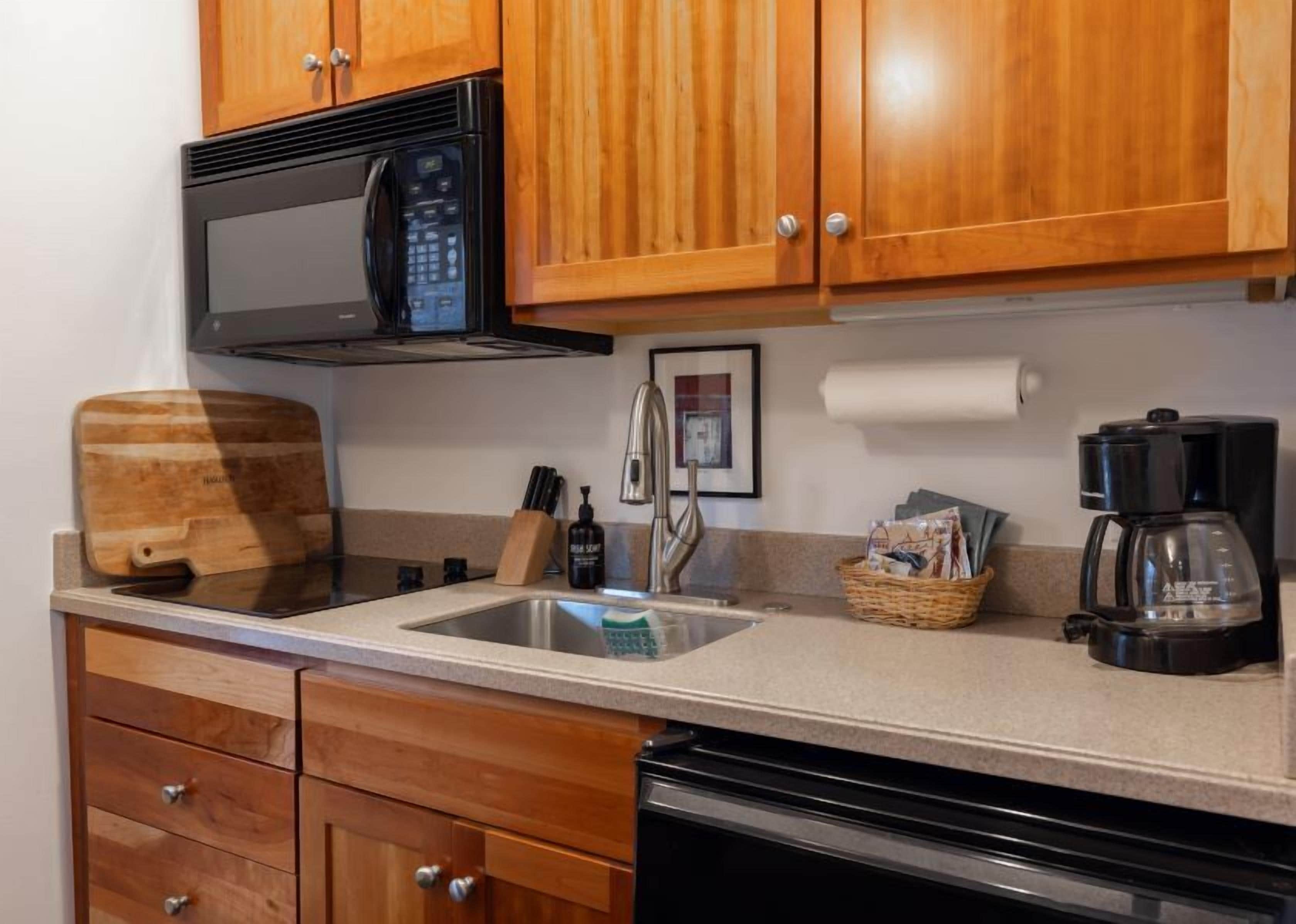 A kitchen with wooden cabinets, a microwave, a coffee maker, a cutting board, and a sink.