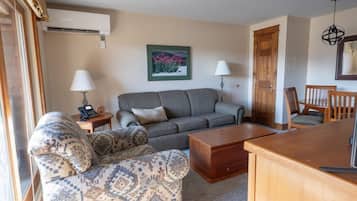 A living room with a sofa, patterned armchair, wooden coffee table, and a dining area with a chair and table.