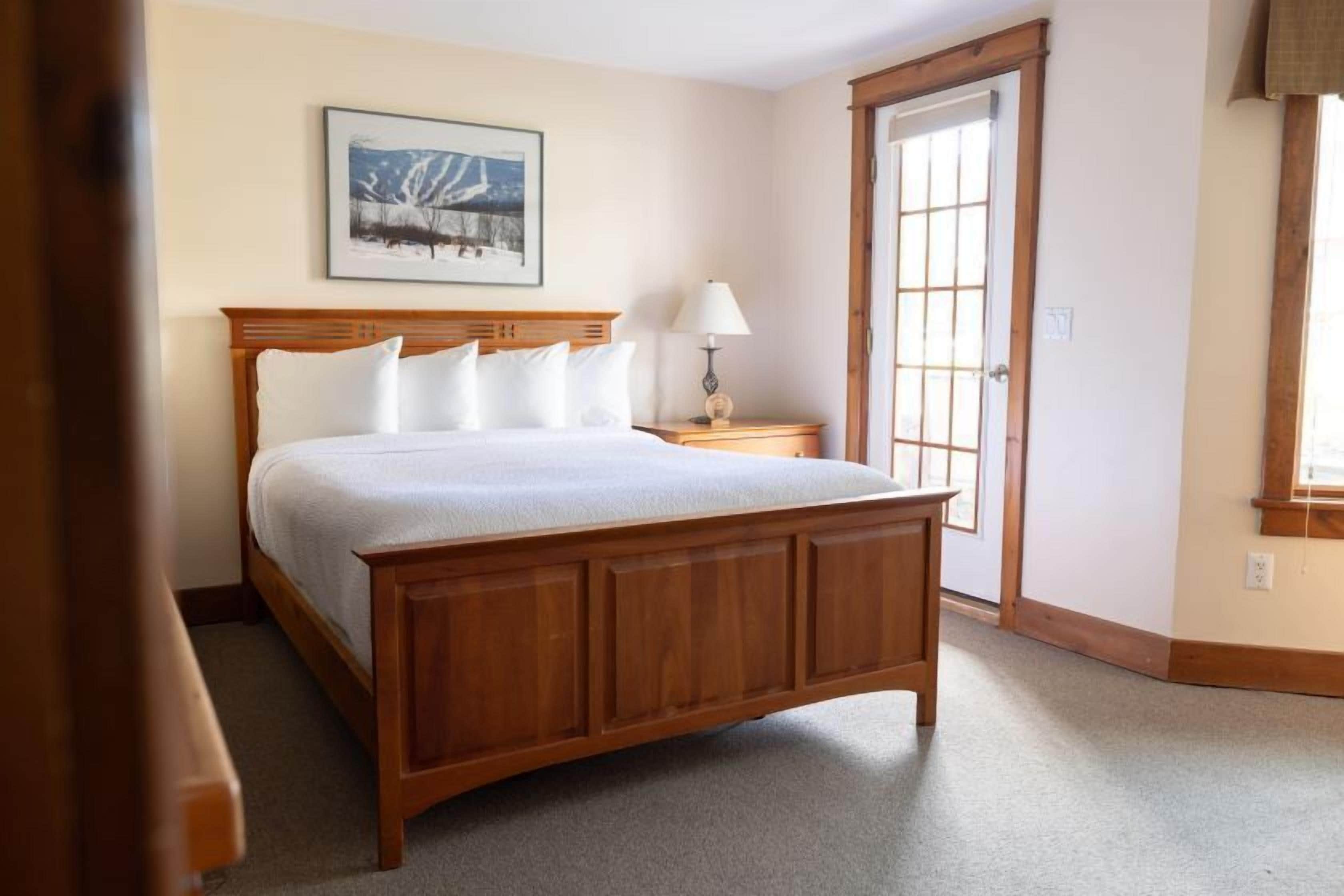 A bedroom with a wooden bed, a nightstand, a lamp, and a door with a window.