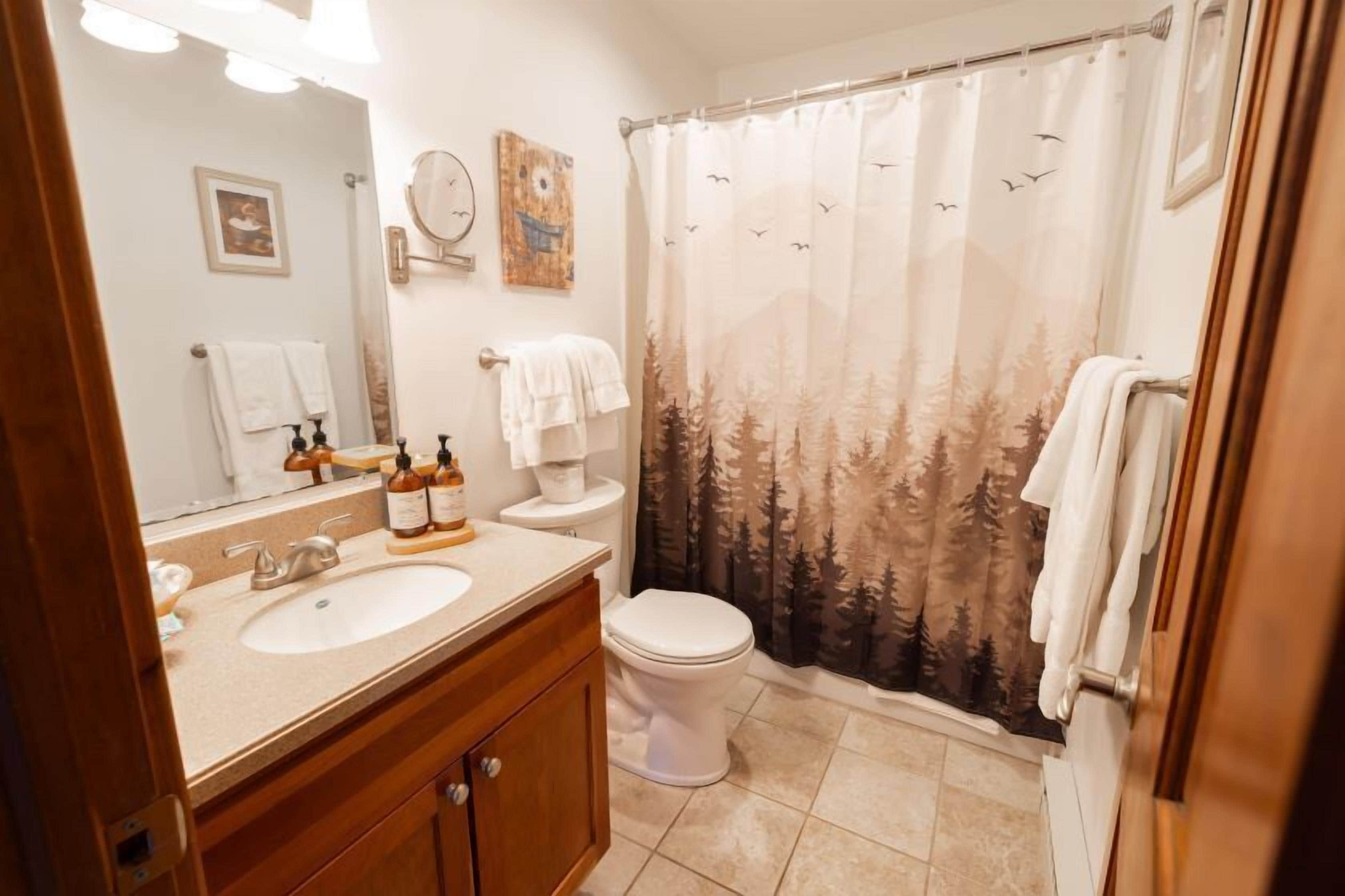 Un baño con lavabo, espejo, inodoro y cortina de ducha con diseño de bosque.
