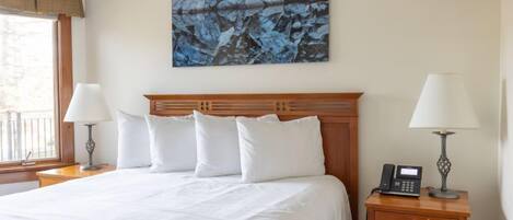 Habitación de hotel con una cama grande, dos mesitas de noche con lámparas, un teléfono y un cuadro en la pared.