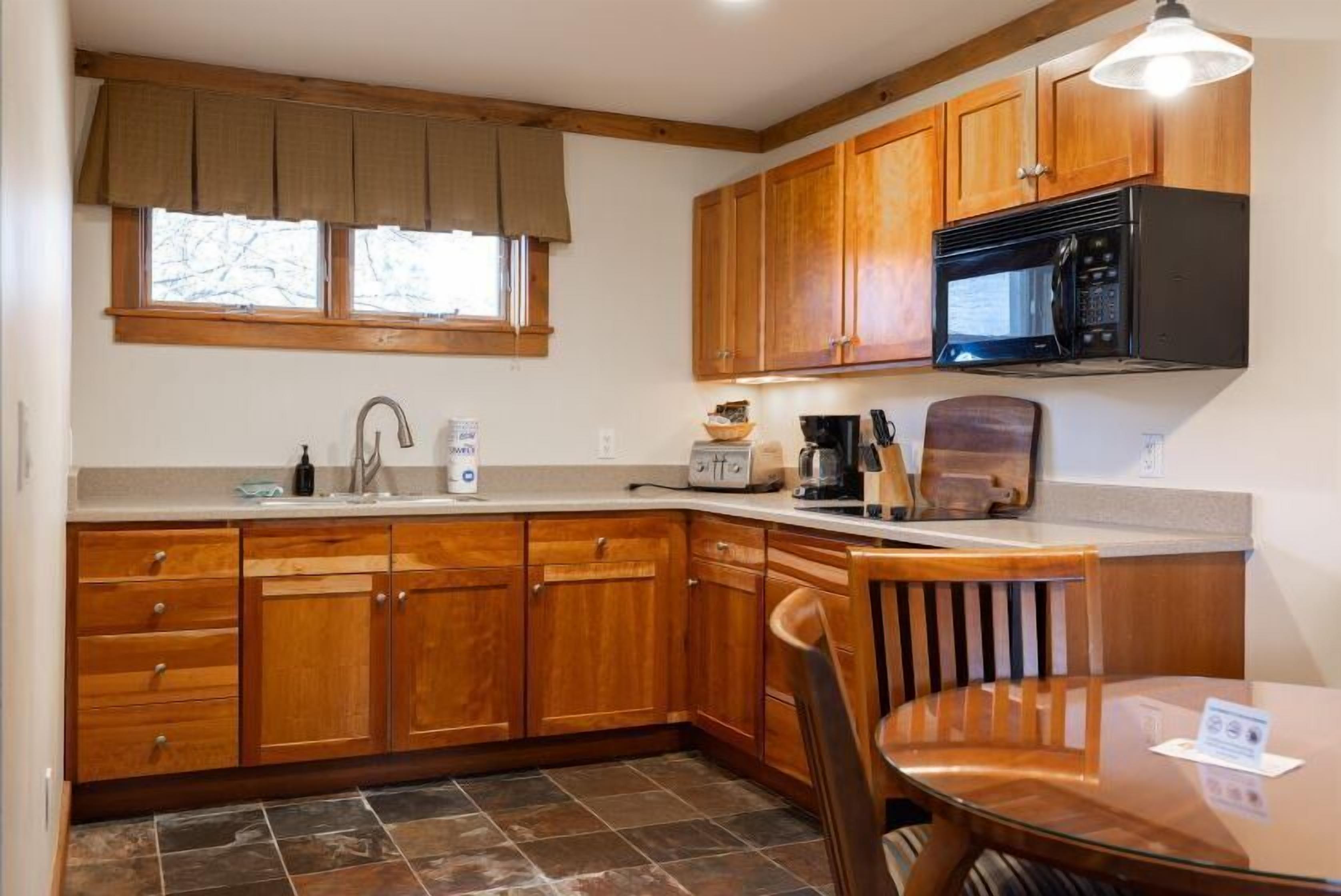 A kitchen with wooden cabinets, a microwave, a coffee maker, and a dining table with chairs.