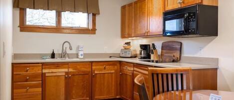 A kitchen with wooden cabinets, a microwave, a coffee maker, and a dining table with chairs.