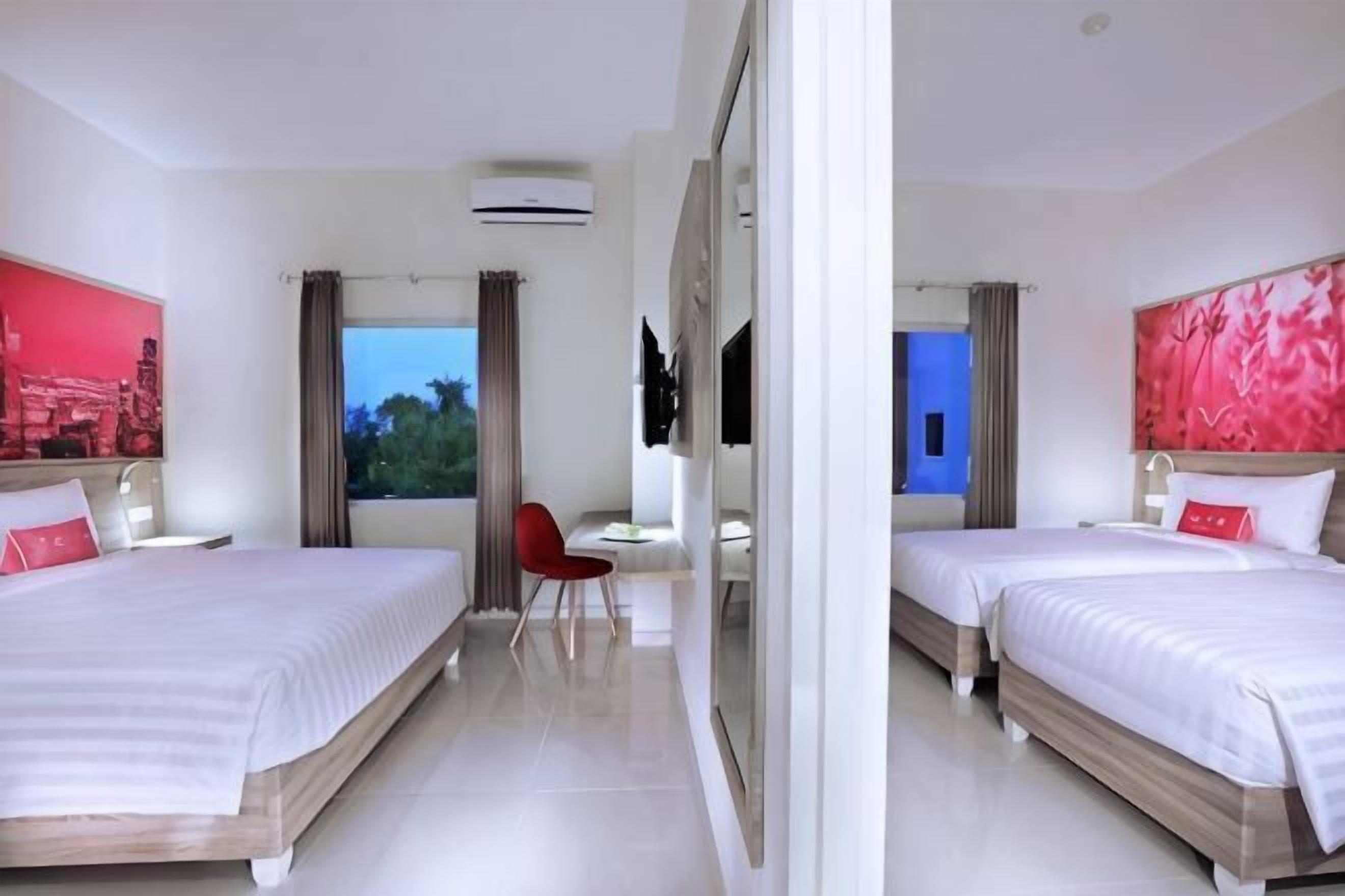 Habitación de hotel con dos camas, un escritorio, una silla y un ventanal grande.