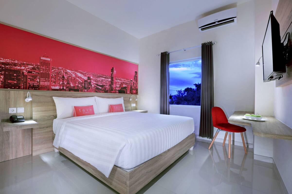 A modern hotel room with a large bed, a desk, and a cityscape view.