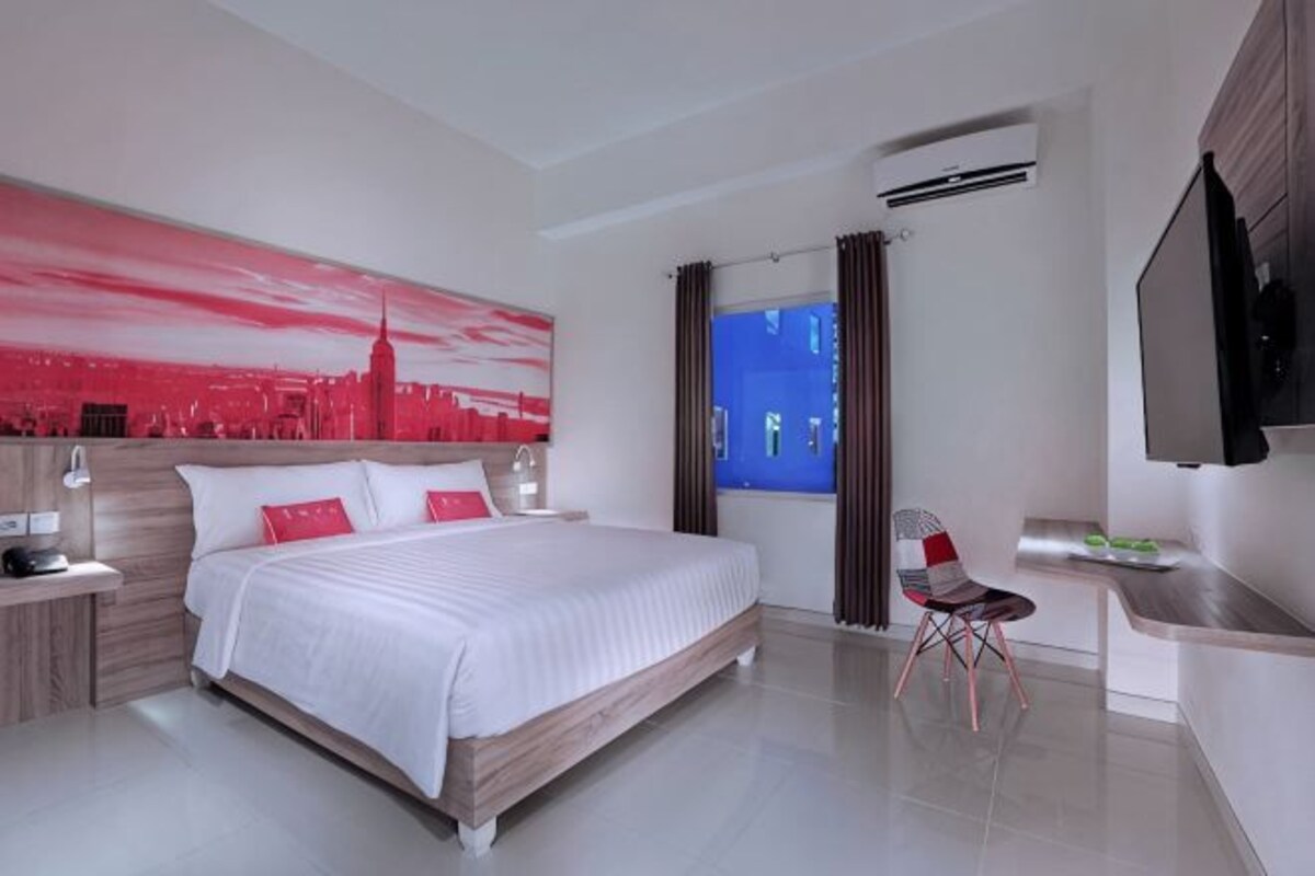 Una habitación de hotel moderna con una cama grande, un escritorio, un televisor de pantalla plana y un cuadro de un paisaje urbano en la pared.