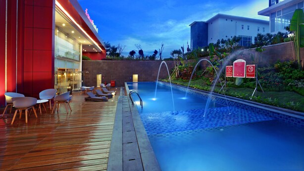 Un hotel moderno con piscina, mobiliario exterior y un jardín bien cuidado.