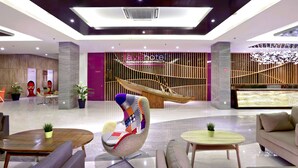 Un vestíbulo moderno de hotel con un área de estar central, un mostrador de recepción y una escalera.