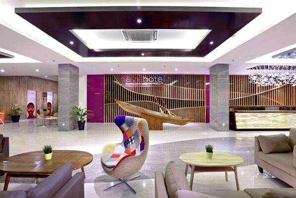 Un vestíbulo moderno de hotel con un área de estar central, un mostrador de recepción y una escalera.