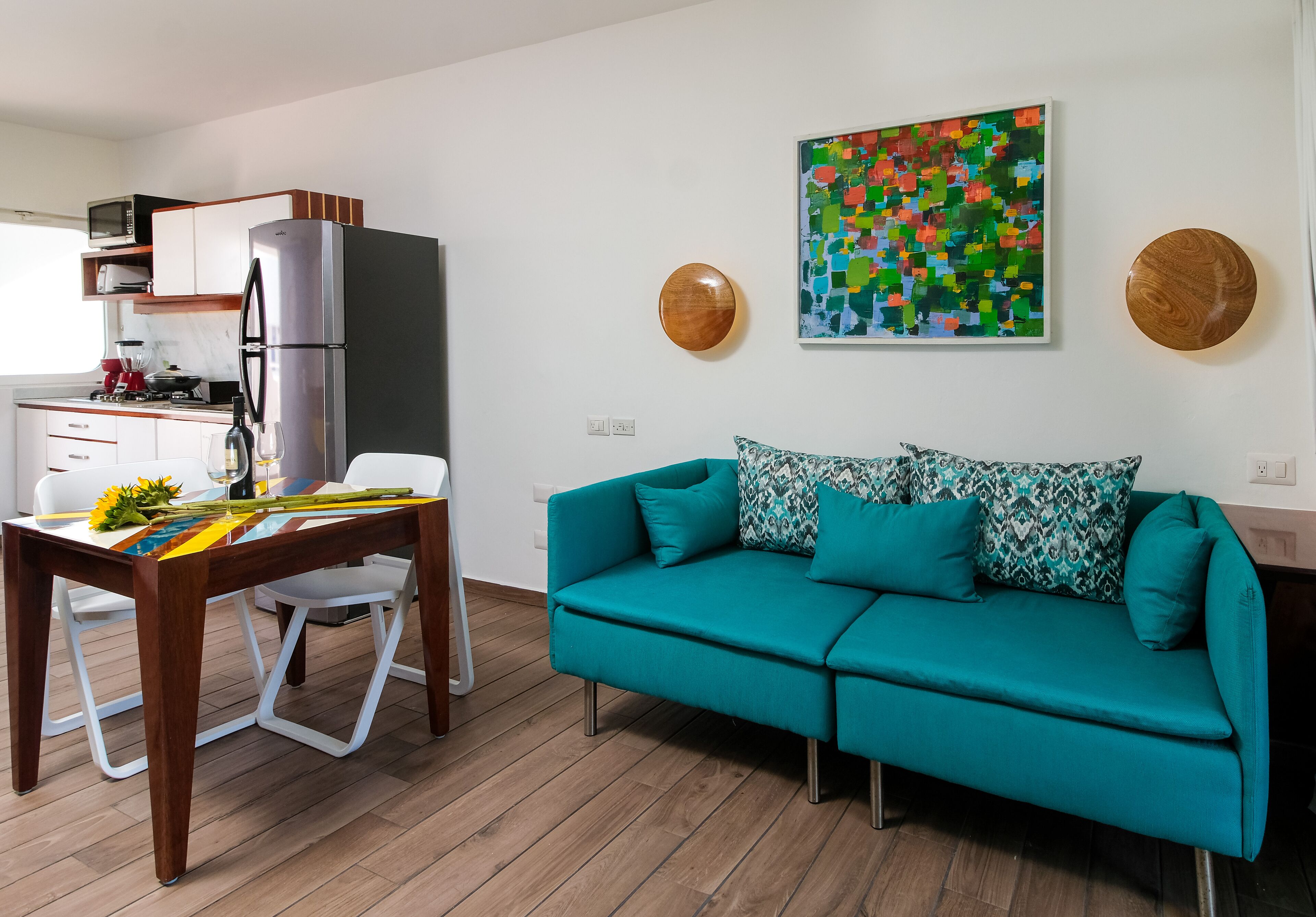 Una cocina moderna con refrigerador, microondas y estufa. Hay un sofá color turquesa y una mesa de comedor con sillas.
