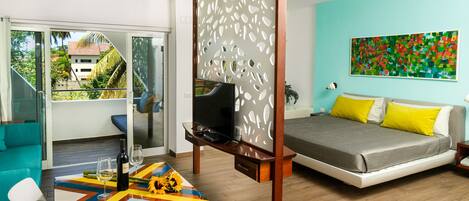 A modern hotel room with a balcony, a TV, a bed with yellow pillows, and a colorful table.
