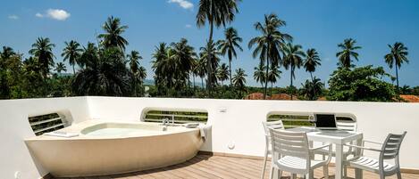 A sunlit outdoor deck with a hot tub, white chairs, and a table.
