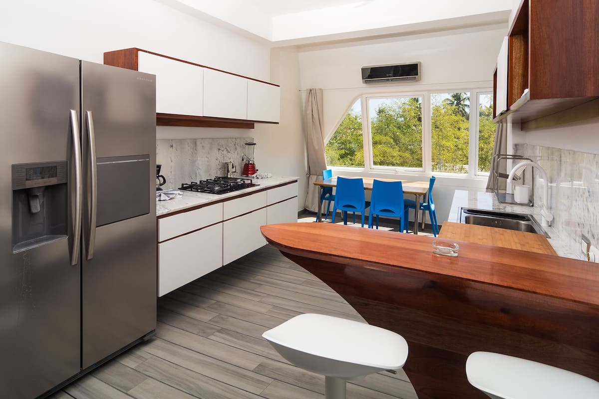 A modern kitchen with a stainless steel refrigerator, a wooden island, and a dining area with blue chairs.