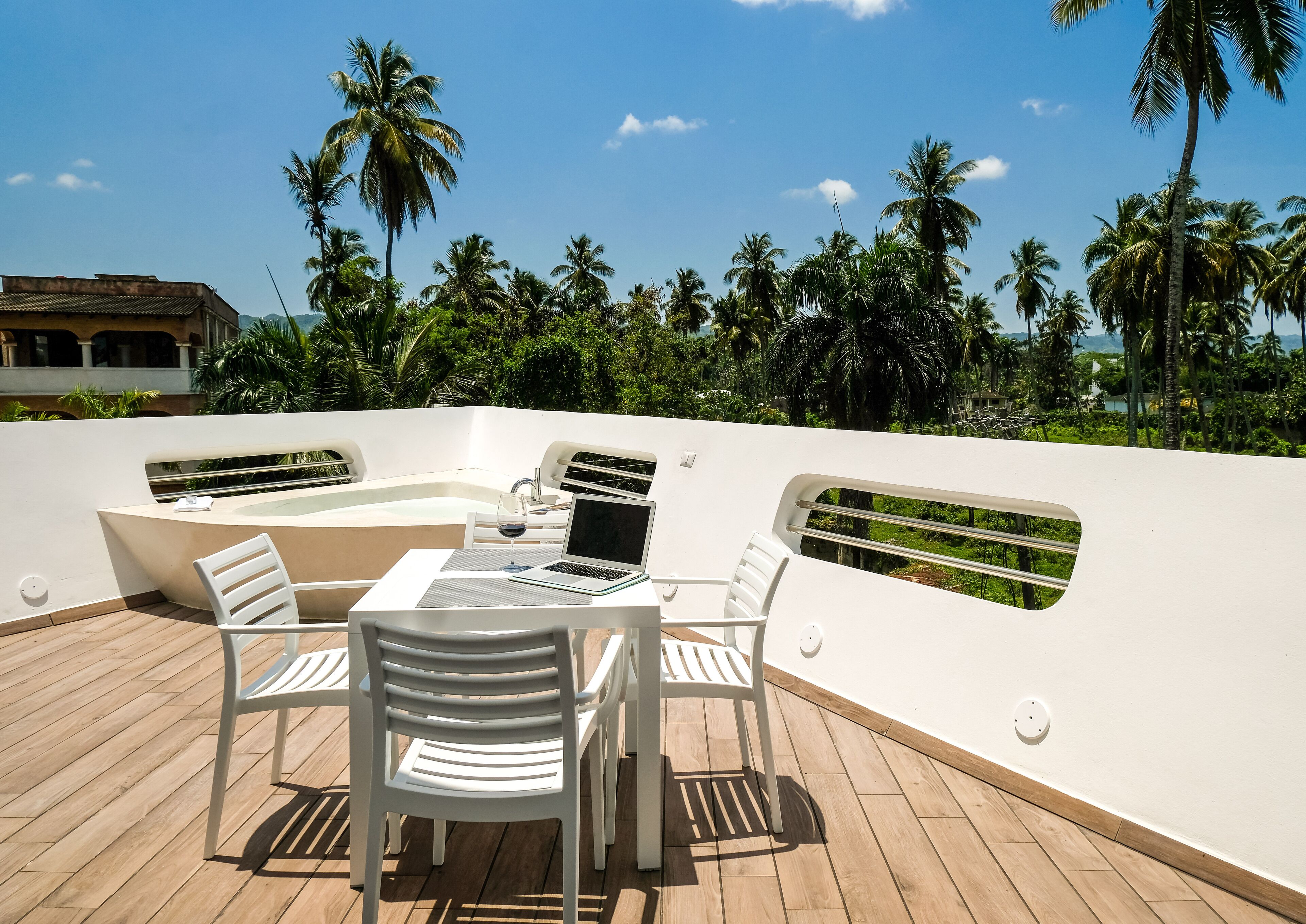 A sunlit outdoor seating area with a table and chairs, a laptop, and a glass of wine.
