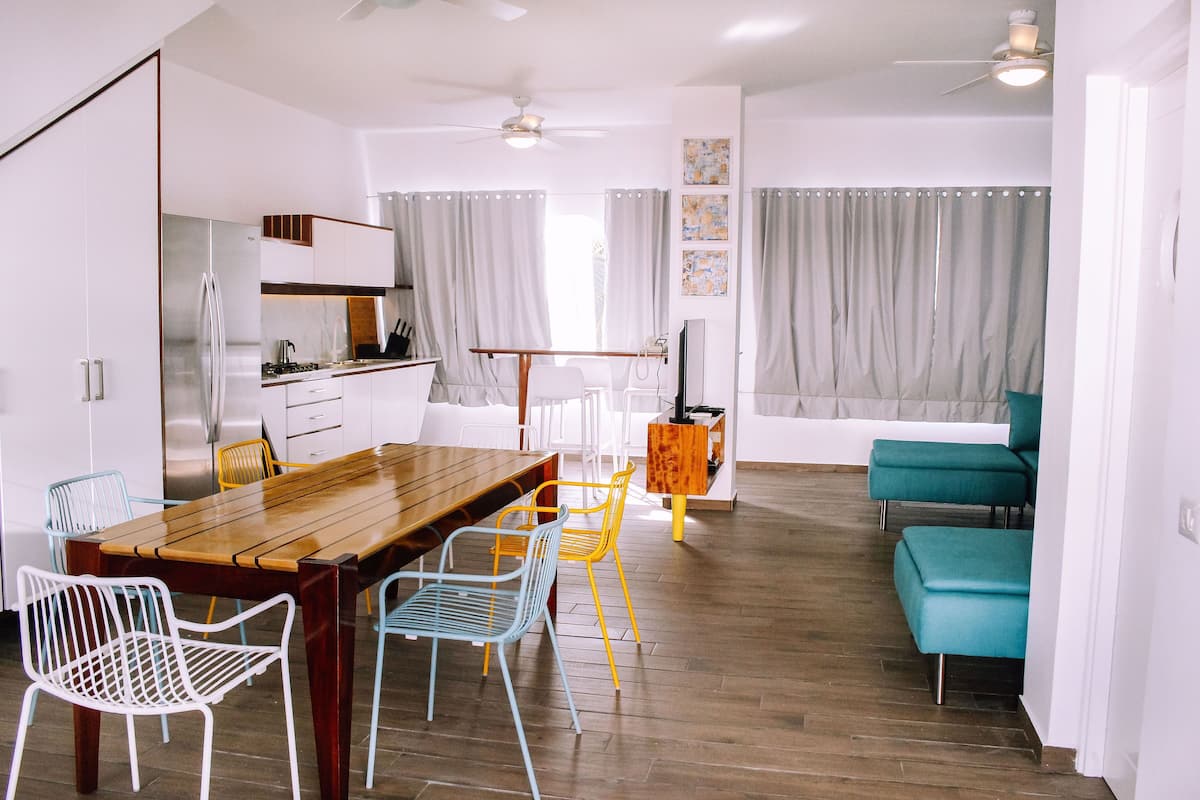 A modern kitchen with white cabinets, a stainless steel refrigerator, and a wooden dining table.